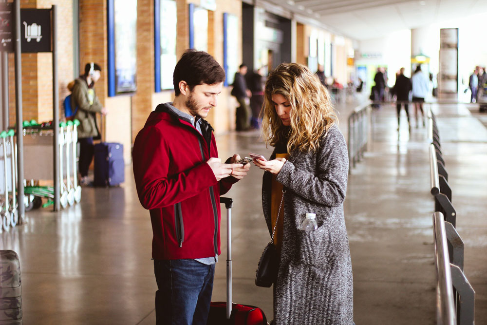 A man and a woman checking their mobile phones at an airport